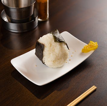 A scrumptious onigiri wrapped in nori, beautifully plated with a pickle on a dining table.