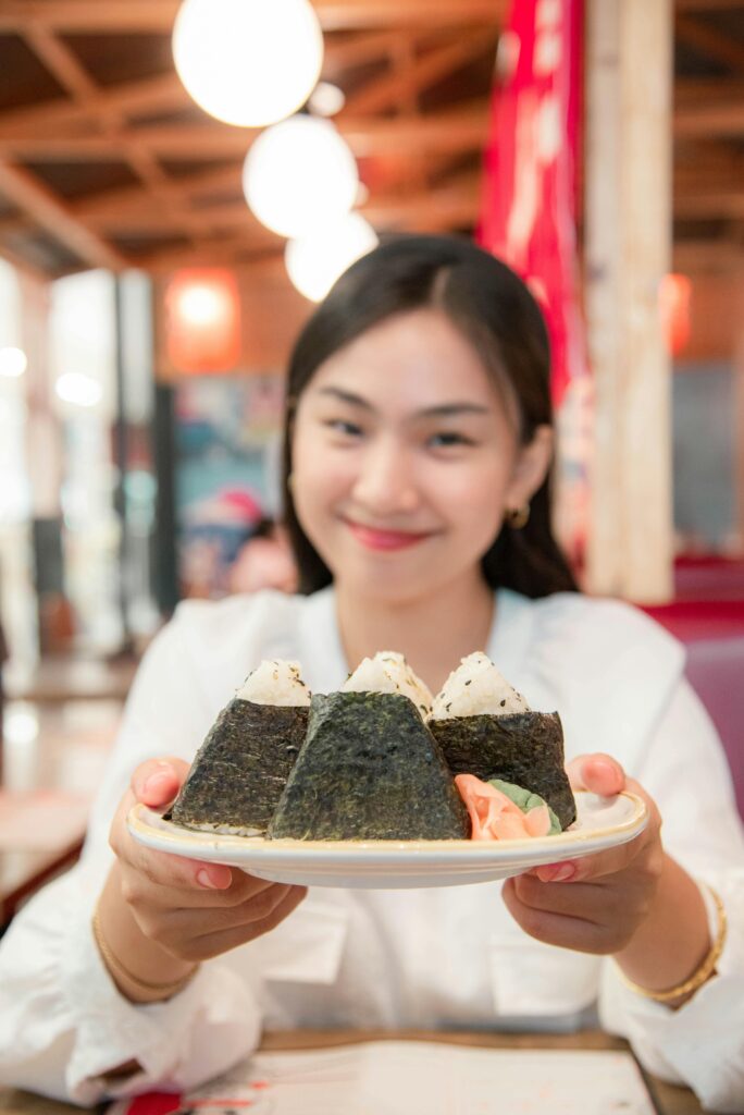 Asian woman presenting a plate of onigiri at a Japanese restaurant. Perfect shot of authentic cuisine.